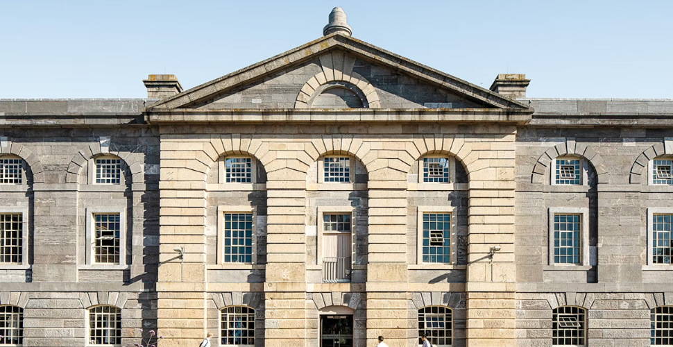 A historic stone building with arched windows and a central pedimented entrance against a clear blue sky.
